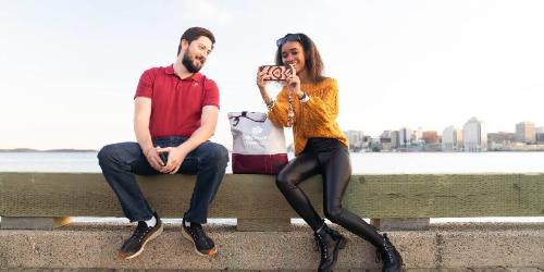 A man and woman using a phone and taking a selfie while sitting on the waterfront