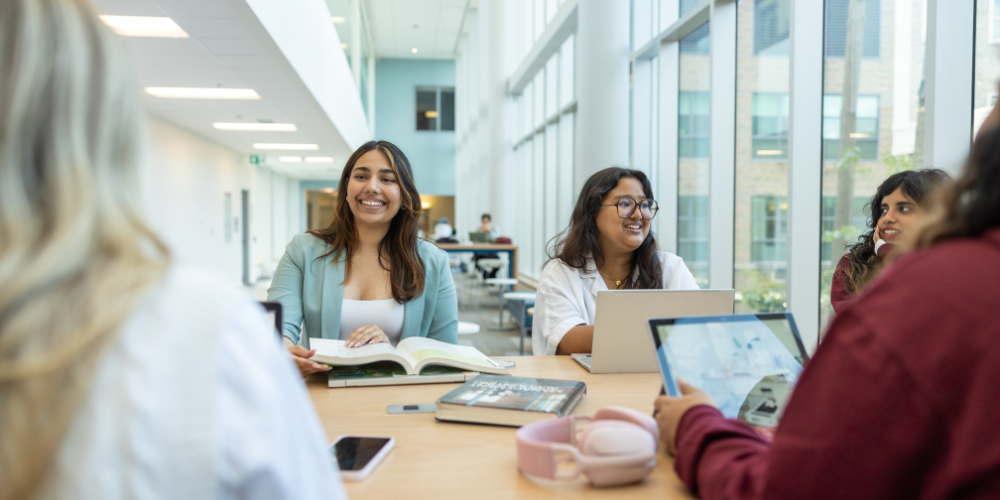 Students sit around a table with laptops as they work together and converse