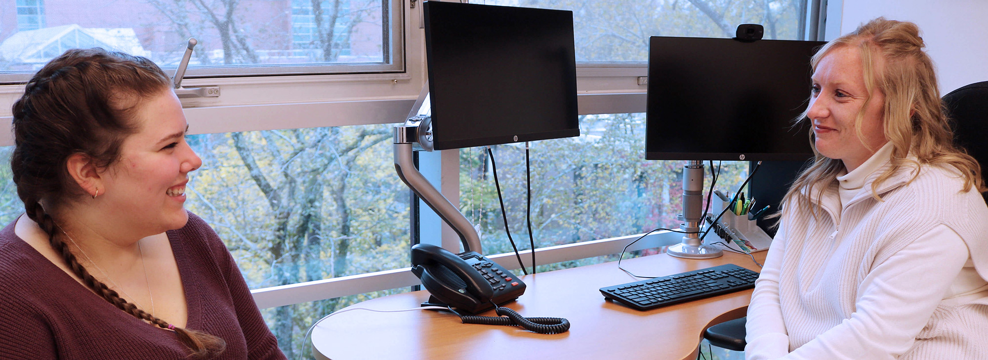 Two people talking near some computer screens.