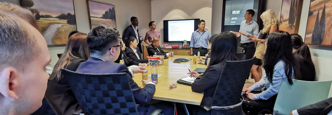 A group of students and business people gather around a table on a corporate tour.