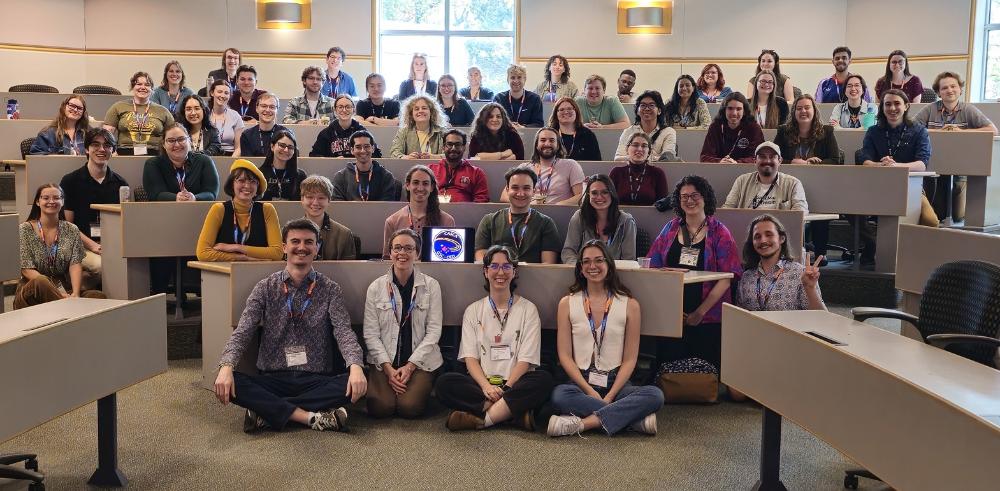 Grad students sitting in a classroom and on the floor for a group picture