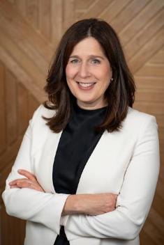 Dale Noseworthy: white skin, long brown hair, confident smile, arms crossed, white blazer and black shirt.