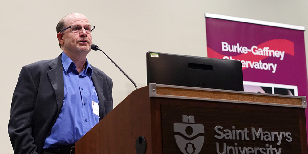 David, a white man with glasses, speaks into a Saint Mary's podium