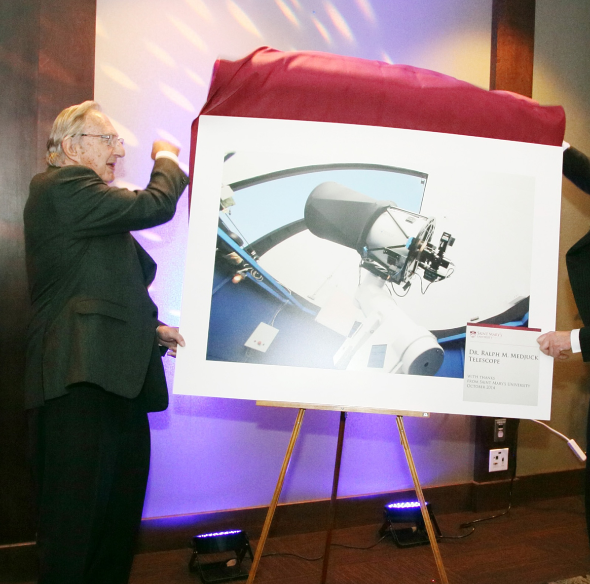 An older gentleman unveiling a photograph of a telescope