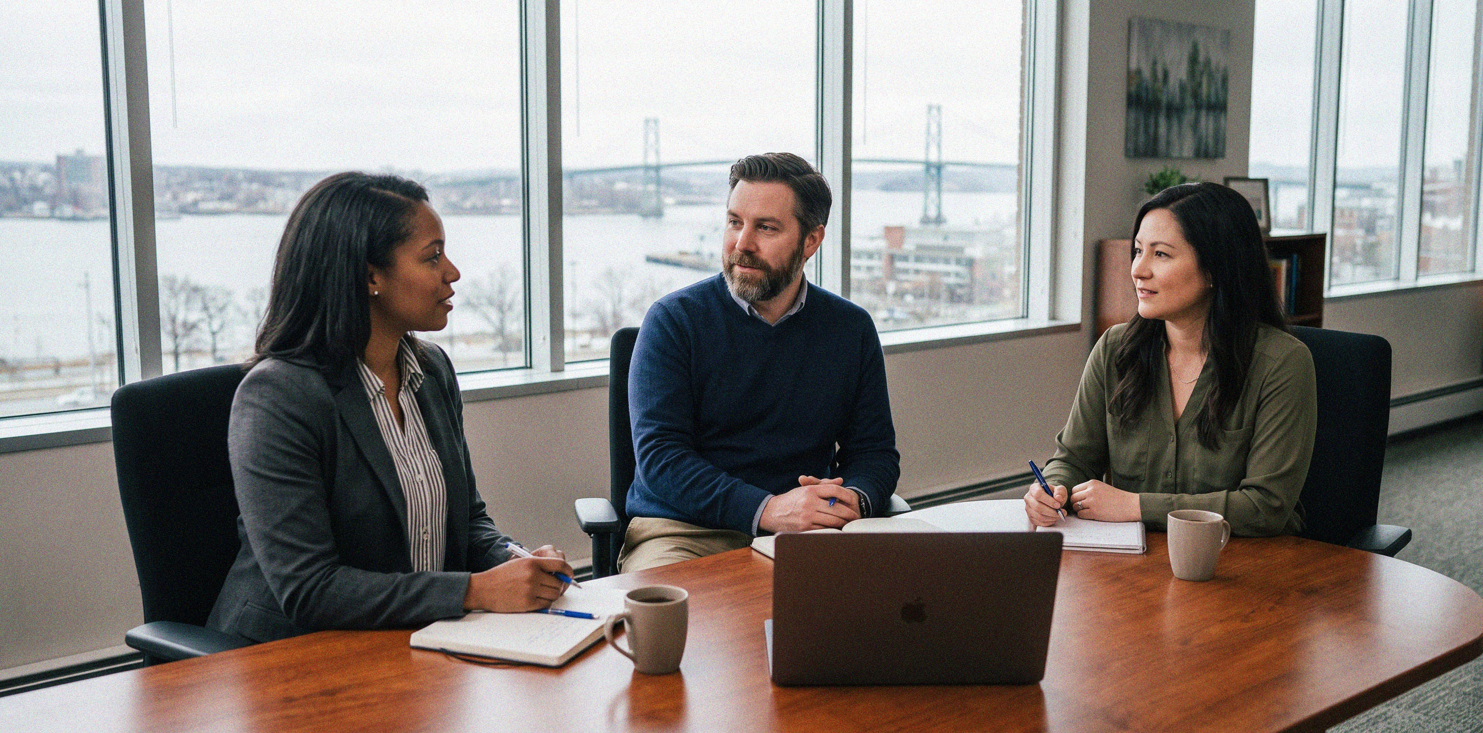 An office meeting of three people with Halifax Harbour in the background.