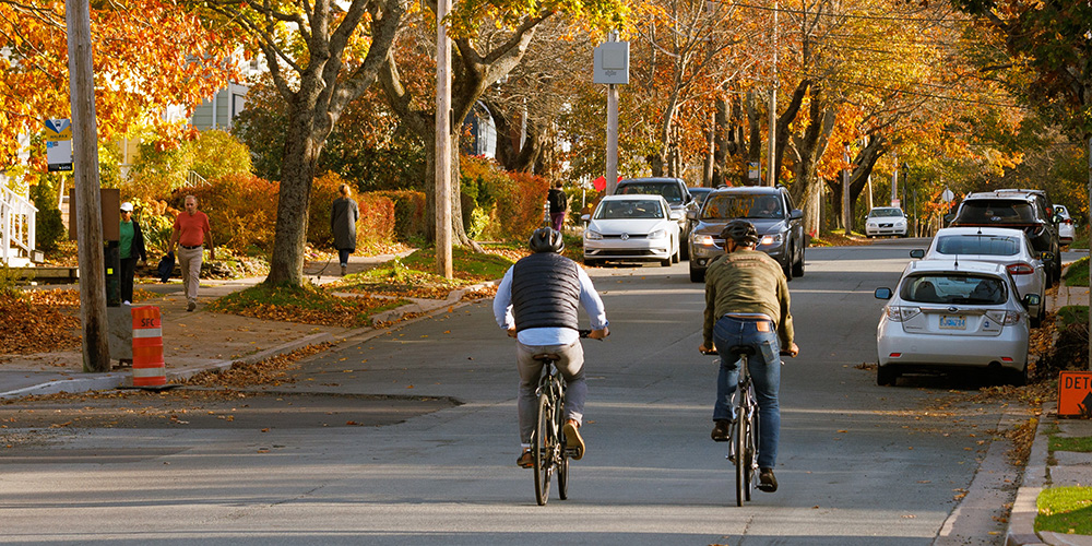 Two people cycling along a street as others walk on sidewalks.