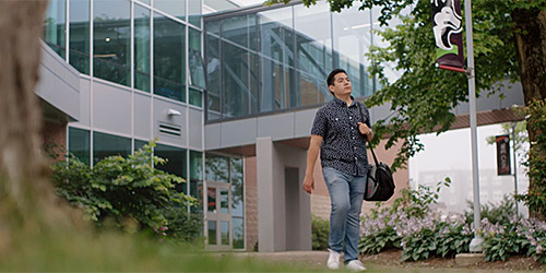 A person with a shoulder bag walking past a SMU banner on a flagpole.